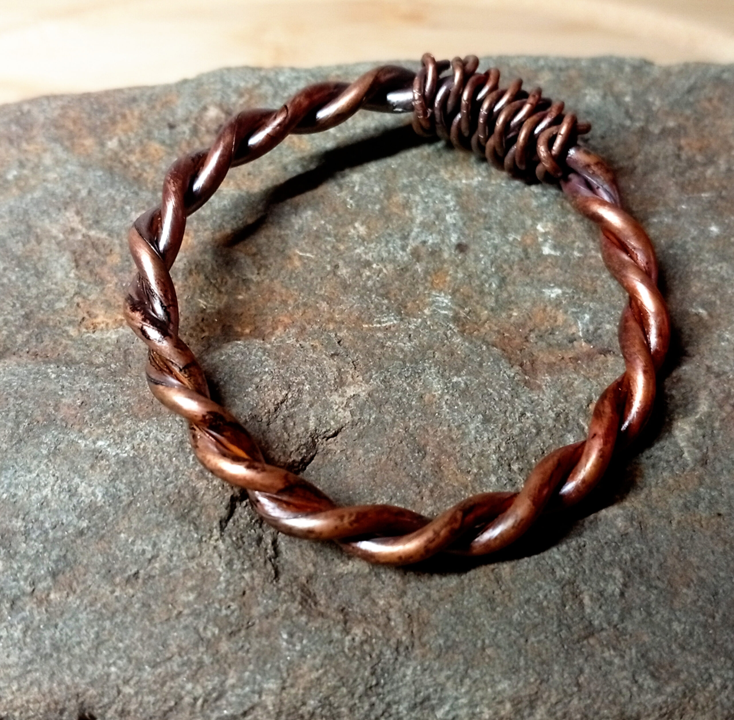 Close-up of twisted Bronze-Oil copper tensor ring on stone