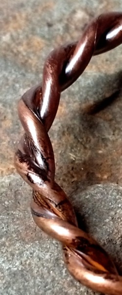 Close-up macro photograph of a twisted raw copper tensor ring.