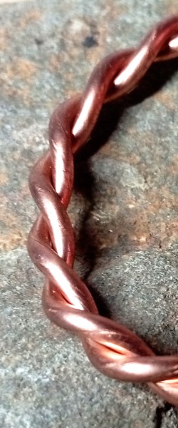 Close-up macro photograph of a twisted raw copper tensor ring.